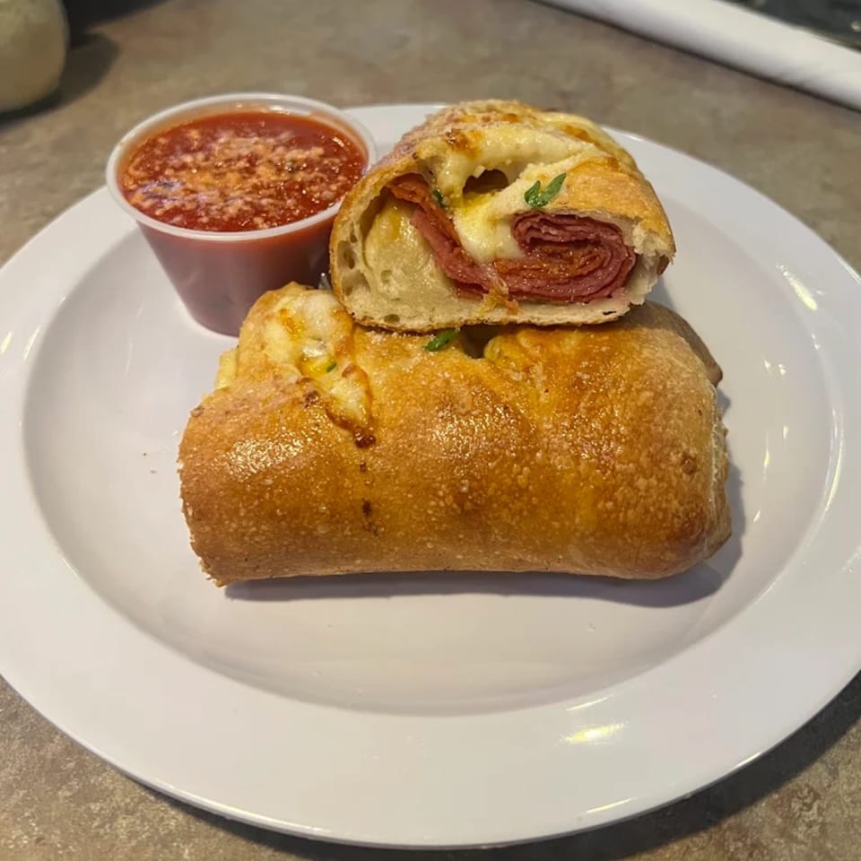 Angelo's West pepperoni stromboli, sliced open to show melted cheese and pepperoni, with a side of marinara.